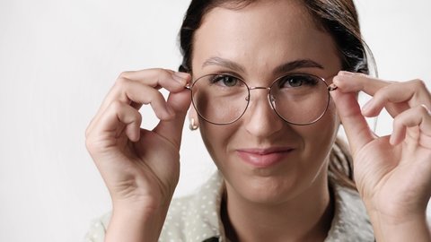 Woman takes off her glasses. Positive woman on white background takes off eyeglasses and smiles while looking at camera. Close-up and slow motion