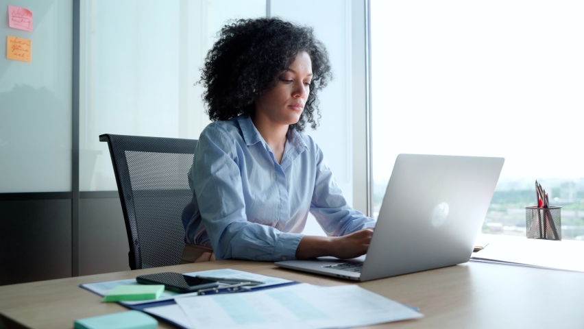 Young African American focused female executive manager businesswoman sitting at desk working typing on laptop computer in contemporary corporation office. Business technologies concept. | Shutterstock HD Video #1078649789