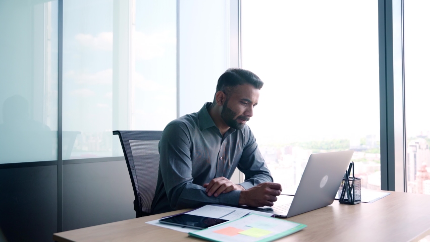 Indian latin successful thoughtful businessman leader thinking of future corporate successful plan ideas using laptop at office desk looking at panoramic view window of building of modern corporation. | Shutterstock HD Video #1078649795