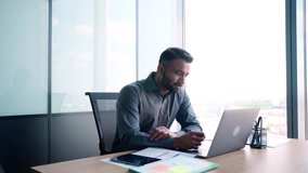 Indian latin successful thoughtful businessman leader thinking of future corporate successful plan ideas using laptop at office desk looking at panoramic view window of building of modern corporation. - Powered by Shutterstock - Get 15% off with code: PIKWIZARD15