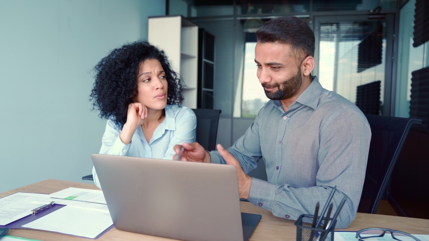 Cheerful multiethnic colleagues male indian manager and African American female businesswoman sitting at desk with laptop working discussing project together having fun. Corporate business concept. Royalty-Free Stock Footage #1078649810