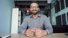 Happy indian businessman in glasses talking to camera at work by video call conference. Financial advisor executive consulting client remotely online in modern office looking at camera. Webcam view. - Powered by Shutterstock - Get 15% off with code: PIKWIZARD15