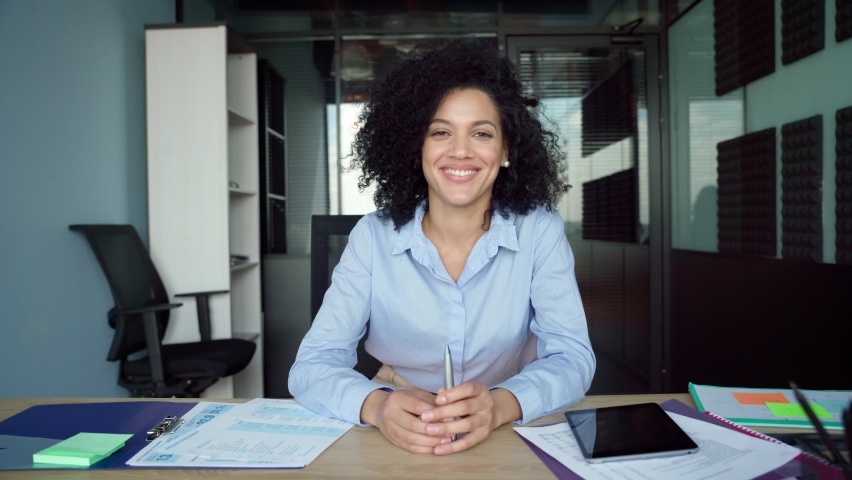 Happy African American businesswoman talking to camera at work by videocall conference. Financial advisor executive consulting client remotely online in modern office looking at camera. Webcam view. Royalty-Free Stock Footage #1078649831
