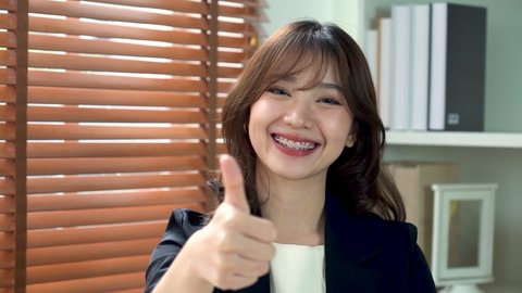 Young Asian businesswoman wearing braces smiles and gives thumbs up. The concept is happy with success.
