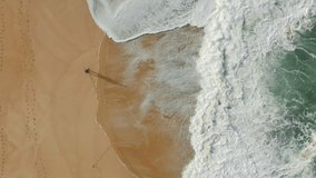 Aerial footage of a man walking along sandy beach. Picturesque seascape with foamy low tide as seen from above. High quality 4k footage