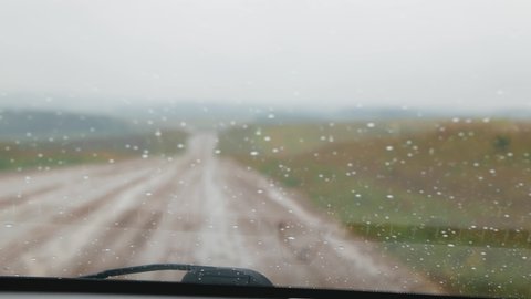 Process of driving in rainy day on country road. Windscreen wipers remove raindrops from windshield while car moves on country road.