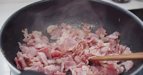 close up view of person roasted chopped crispy bacon strips slices in a Hot Skillet frying pan with hot oil splashing, rich in fat and color, sizzling and smoking, morning breakfast
