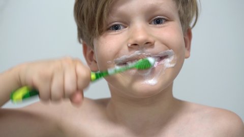 cheerful little boy brushing teeth in front of the bathroom mirror
