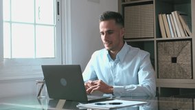 Happy young caucasian millennial businessman working at home at desk with laptop or computer having fun. Young male person in video conference taking care of the business or market.
