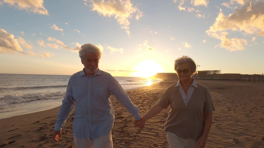 Portrait of couple of mature and old people enjoying summer at the beach looking to the sea smiling and having fun together with the sunset at the background. Two active seniors traveling outdoors.
 Royalty-Free Stock Footage #1078676375