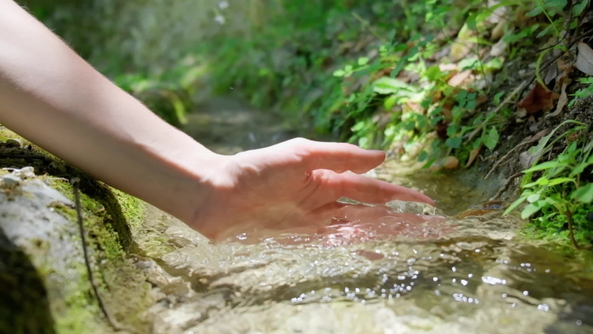 Female hand touching fresh spring water in forest creek, slow motion of pure stream water.