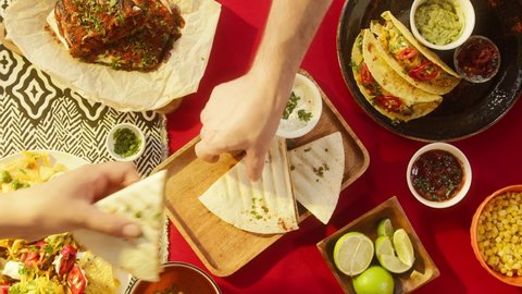 Traditional Mexican food, tex mex cuisine. Hands taking cooked quesadilla from wooden tray and dipping into sauce, tacos served with meat and vegetables, tomato soup with cilantro, guacamole.
