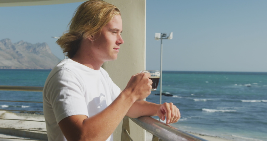 Animation of social media icons and numbers flying over caucasian man drinking coffee by seaside. global social media, communication and connection concept digitally generated video.