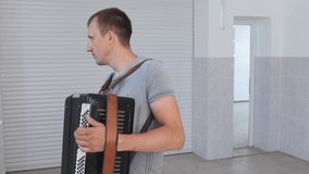 Young attractive man plays a musical instrument indoors. Passion for accordion, playing keyboard equipment as a hobby.
