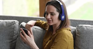 Attractive young woman wear headphones using smart phone take part in video call, enjoy personal conversation with friend or family. Remote communication, modern wireless tech usage, comfort concept