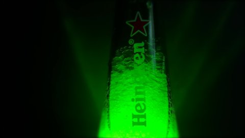 Moscow, Russia - 09.05.2021: Beer bottle neck full of beer foam, condensation drop on beer bottle. Heineken Lager Beer on dark background. Halloween party concept. Night bar. Saint Patrick's day