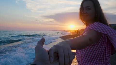 Young cute woman holds man's hand and drag. First view person POV. Walk on sea beach on sunset background. Face with smile face, enjoy and happiness. Follow me, invite concept. Husband and wife