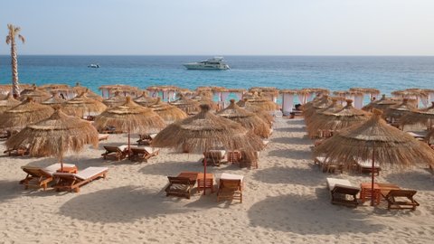 Beautiful beach with umbrellas and sunbeds. Perfect summer vacation destination. Straw sunshades and sunbeds on the empty beach with sea in the background. 