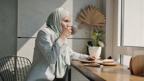 Portrait of charming muslim lady drinking coffee and enjoyng view from cafe window smiling feeling happy and relaxed. Lifestyle and people concept.