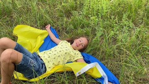 4k Small girl lies on Ukrainian flag in the meadow