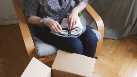 Paris, France - Circa 2021: Overhead of curious woman unboxing unpacking new Crocs pairs of shoes sandals in her living room - online e-commerce shopping