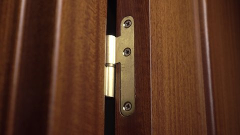 Old rough golden hinge of a brown dark wooden room door. Opening and closing with the movement of the hardware close-up