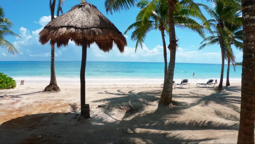 Gorgeous shot walking through a tropical beach with white sand, palm trees, and turquoise water on the beautiful Playa del Carmen in Riviera Maya, Mexico near Cancun on a sunny summer day on vacation. Royalty-Free Stock Footage #1078714370