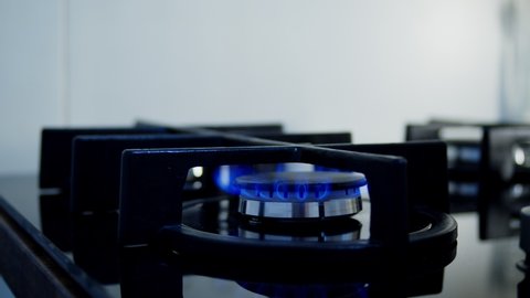 Unrecognizable woman hand keeping lighter, turning on stove switch, lighting kitchen burner of gas stove indoors. Stove burner igniting into blue cooking flame. Natural gas inflammation