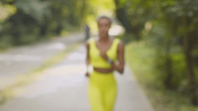 Blurred young african american woman running to camera and smiling, working out alone in public park, slow motion