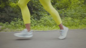 Active lifestyle concept. Young african american lady wearing sportsuit running, training in green public park, side view, tracking shot from legs to head, slow motion
