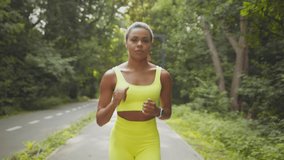 Healthy lifestyle concept. Close u portrait of young sporty african american woman in bright sportsuit running alone in morning, looking at camera, jogging in public park, follow shot, slow motion