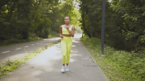 Sport and gadgets. Young african american woman runner stop jogging, looking at her smartwatch and keep running in park, checking her activity on device, slow motion