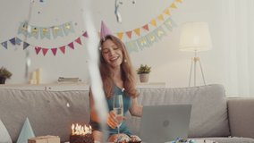 Happy holiday on distance. Young cheerful lady celebrating birthday with friends online, drinking champagne and dancing under confetti, tracking shot, slow motion