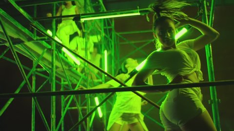 Many female dancers dressed in white shorts dancing inside abandoned building in high multistage  construction . Stylish Girls dancing, twerking , doing gymnastic movements , jumping . Slow motion 

