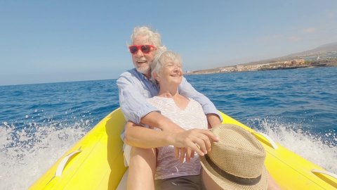 Beautiful and cute couple of seniors or old people in the middle of the sea driving and discovering new places with small boat. Mature woman holding a phone and taking a selfie with hew husband
