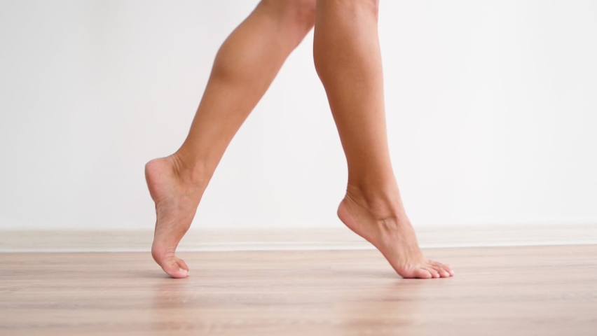 Close-up, slender female bare feet are walking against background of a white wall. Attractive legs an unrecognizable woman gracefully walk on tiptoes around apartment. Foot and body care concept. | Shutterstock HD Video #1078722815
