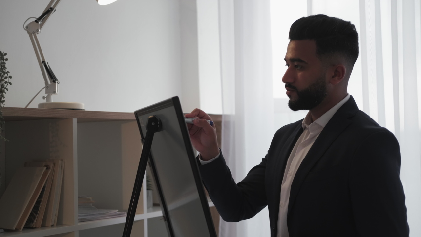 Business courses. Handsome man. Task notice. Work presentation. Confident oriental guy in elegant suit concentrating on writing information on chart board in light room interior copy space.