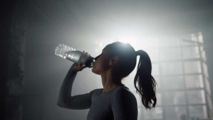 Portrait of tired woman in sportswear drinking water from sports bottle in gym. Female athlete replenishing water balance after fitness workout. Relaxed fit girl drink water from bottle in sport club Royalty-Free Stock Footage #1078725209