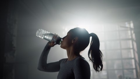 Portrait of tired woman in sportswear drinking water from sports bottle in gym. Female athlete replenishing water balance after fitness workout. Relaxed fit girl drink water from bottle in sport club: stockvideo