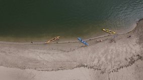 On the sandy beach there are three kayaks of different colors, one yellow kayak swims up to the shore, people in vests with oars, an aerial view from above. Don River. 4K video.
