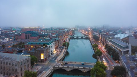 Forwards fly above River Liffey. Aerial hyperlapse footage of evening traffic on waterfront illuminated by street lights. Low clouds above city. Dublin, Ireland