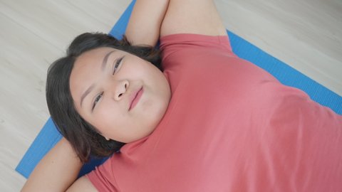 Asian young plus size girl trying to sit up exercise in living room. Attractive oversize big chubby girl fight to lose weight for health care and use mat workout, follow online instruction in house.