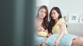 Asian young woman couple watch jump scare movie on television at home. Attractive lesbian friend feel excited and shock while sit on sofa watch scary video on TV in house. Activity lifestyles concept.