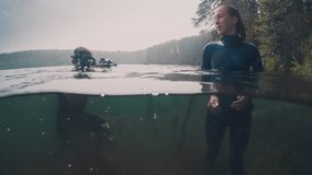 Fashion underwater photographer. Male photographer takes picture of the young model standing in the lake in wetsuit. Diver with underwater camera films model in the water.