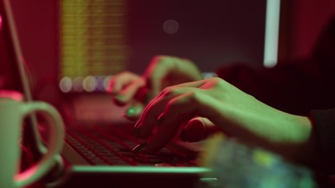 Professional hacker workplace close-up. Female hands typing on keyboard. Technology for hacking computer systems in secret place of work. Laptops and wires at desk in darkness. 