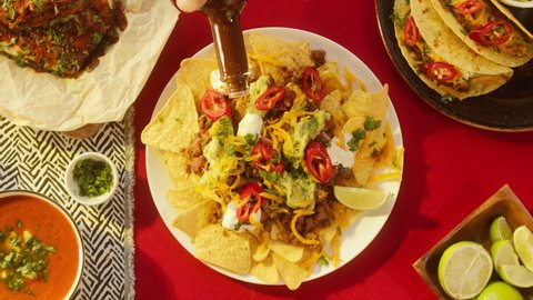 Mexican food, traditional tex mex cuisine. Adding spicy sauce on corn nachos served with meat and vegetables. Tomato soup with cilantro, guacamole. Setting the table with American dishes top view.