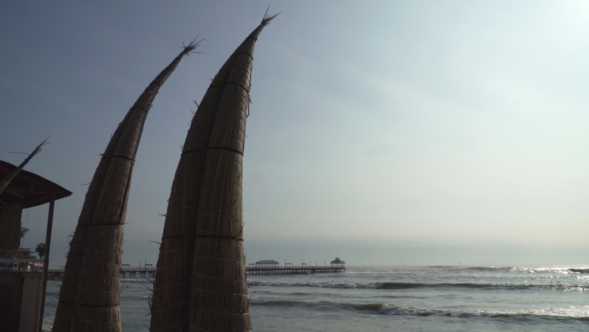 Athentic Caballito de totora Boats Along the Huanchaco Beach in Trujillo, La Libertad, Peru with Muelle de Huanchaco Pier in the Background.