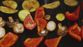 Vegetables cooking on grill pan in vegetarian restaurant kitchen. White champignon mushrooms, red bell peppers, green zucchini being cooked for dinner