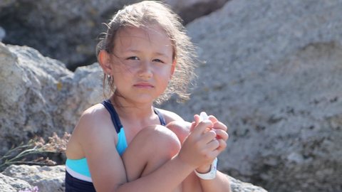 Portrait of beautiful child girl in swimsuit looks at camera on the beach in windy weather. High quality 4k footage