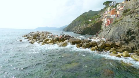 RIOMAGGIORE, ITALY - Jul 07, 2019: The Mediterranean and tourists lying on the rocks on the coast of Riomaggiore in Italy - shot in 4K